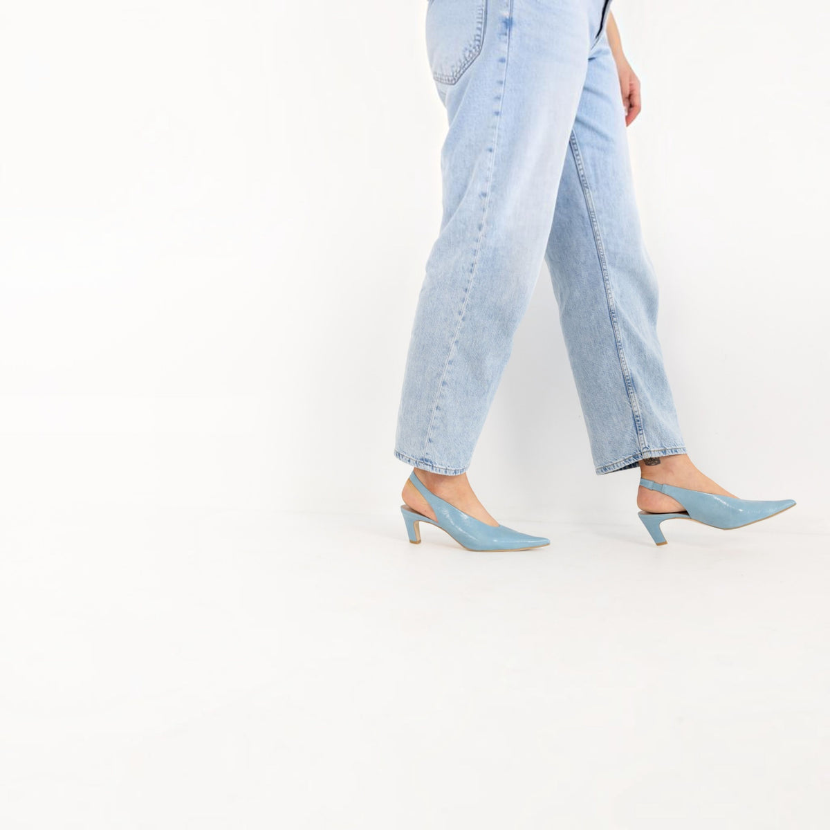Model wearing Celia Blue Pearl leather slingback heels, walking in tailored trousers, by Estela
